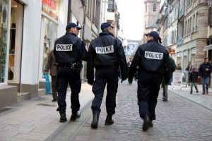 photographie de trois policiers patrouillant dans une rue, de dos