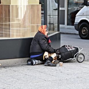 Photographie d'une femme assise au coin d'une rue avec ses paquets