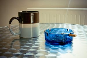 Photographie d'une cigarette qui fume dans un cendrier à côté d'un mug