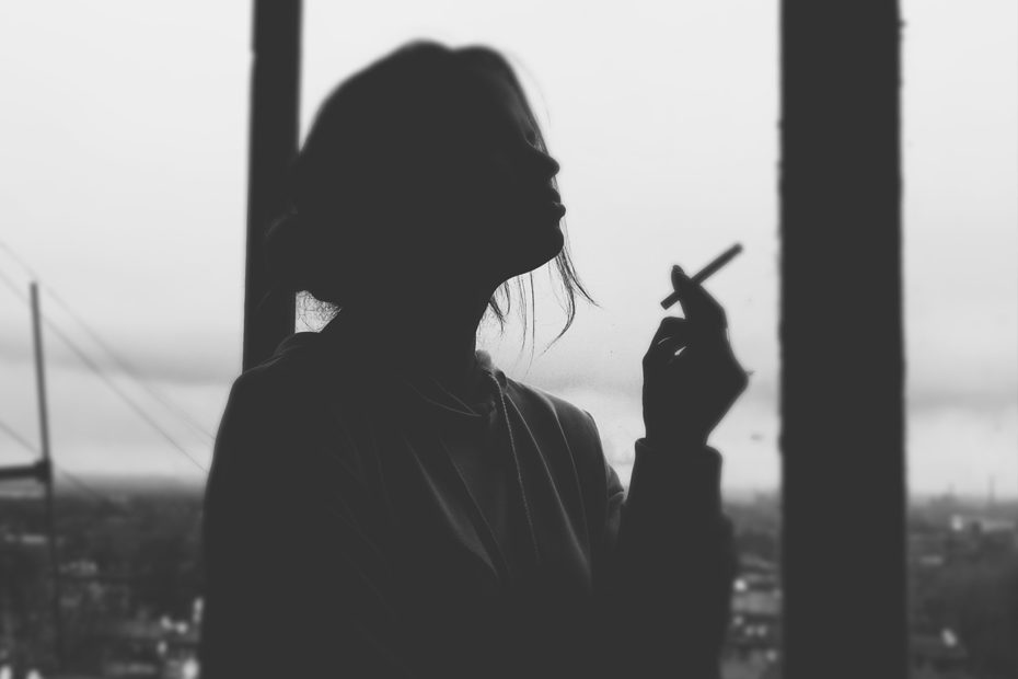 photographie en noir et blanc d'une femme à contrejour en train de faire une pause avec une cigarette
