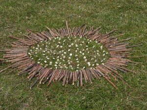 Photographie d'une oeuvre de land art batons et pierres posés en cercle dans l'herbe