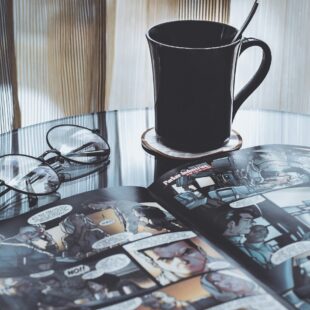 BD ouverte, tasse et lunettes sur une table.