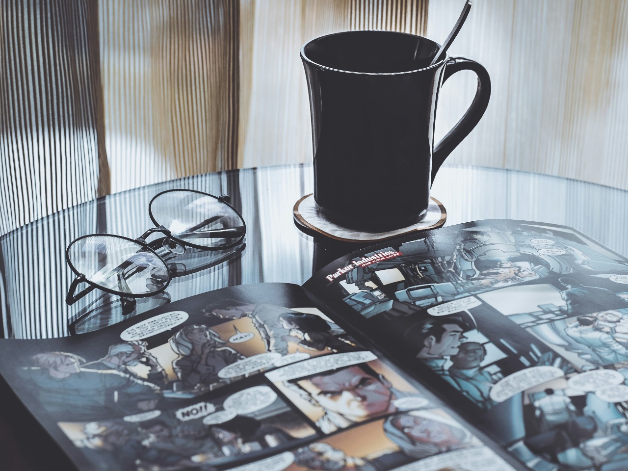BD ouverte, tasse et lunettes sur une table.