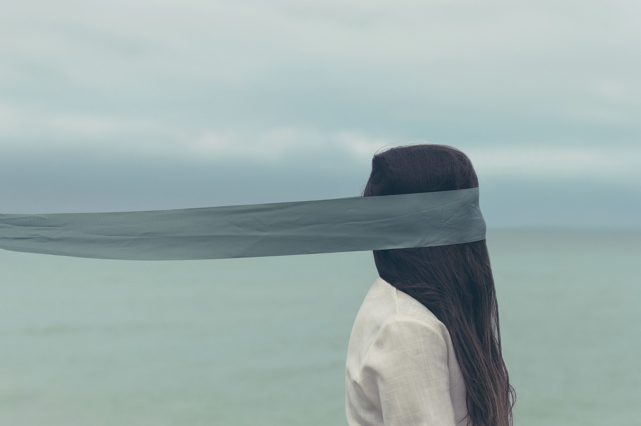 Face à la mer, une femme avec les cheveux qui retombent devant son visage et un ruban autour des yeux