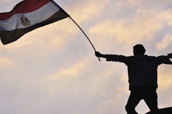 Homme debout dans le crépuscule, levant le drapeau égyptien