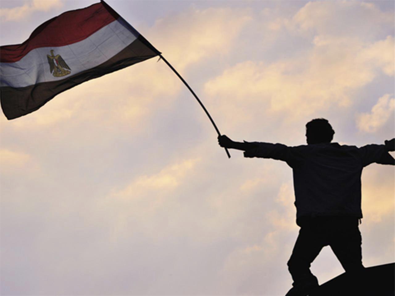 Homme debout dans le crépuscule, levant le drapeau égyptien