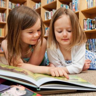 Deux petites filles en train de lire allongées par terre.