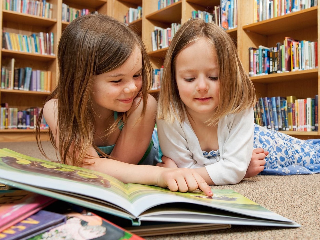 Deux petites filles en train de lire allongées par terre.