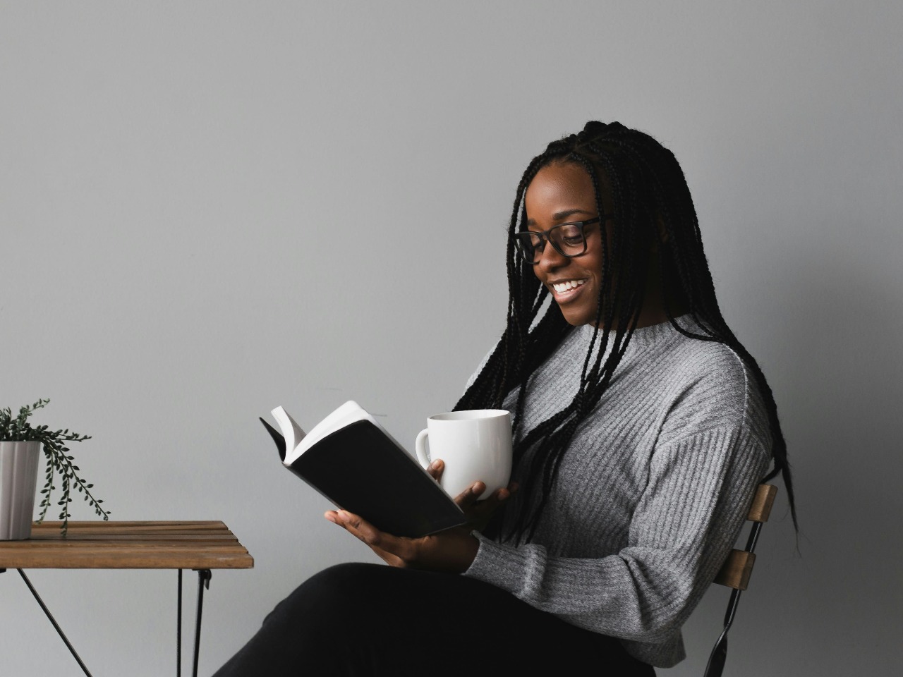 Femme assise en train de lire un livre une tasse à la main.