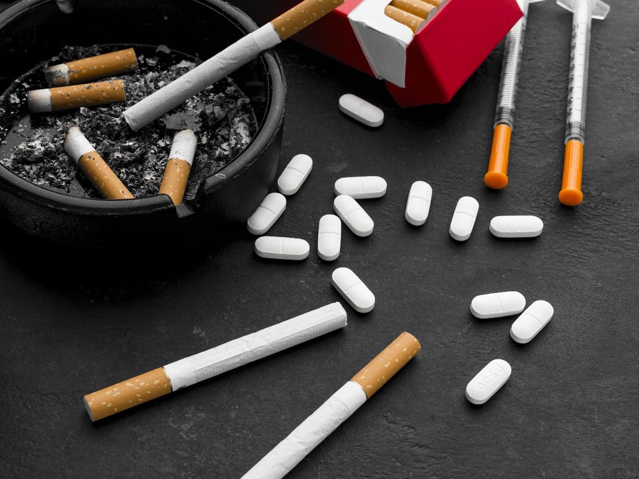 Présentation de produits addictifs posés sur une table , cigarettes, médicaments, seringues