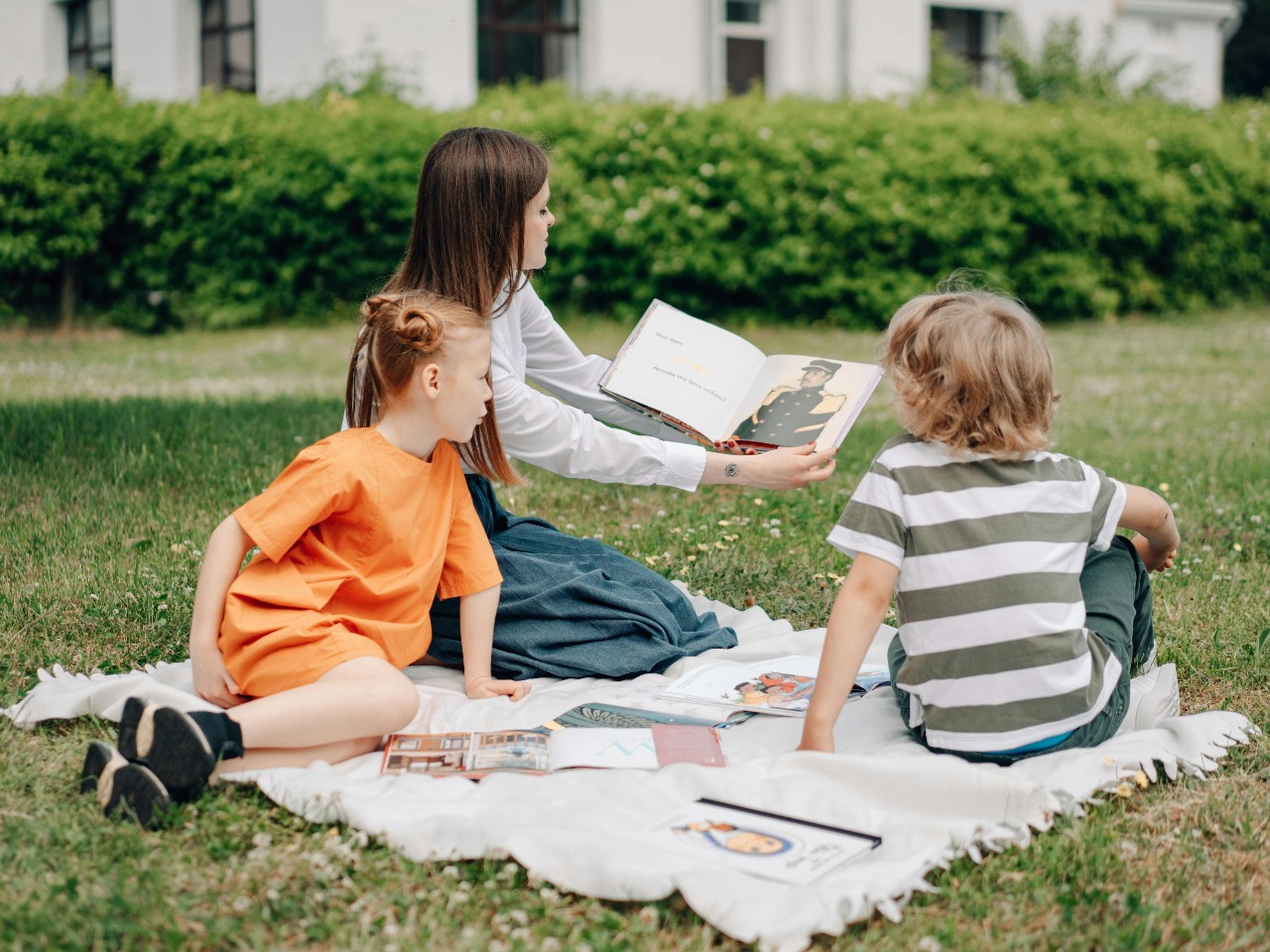 Femme qui lit un livre à deux enfants assis dans l'herbe.