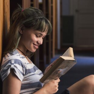 Une adolescente lit un livre assise par terre dans une bibliothèque.