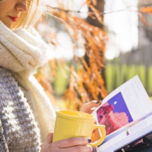 Femme en train de lire à l'extérieur avec une tasse.