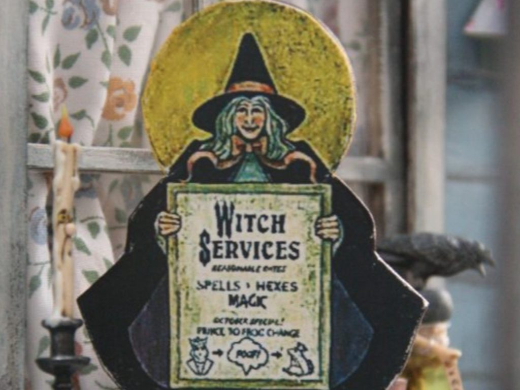 Objet décoratif représentant une sorcière avec une pancarte sur laquelle est proposé un service de transformation de prince en crapaud