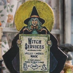 Objet décoratif représentant une sorcière avec une pancarte sur laquelle est proposé un service de transformation de prince en crapaud
