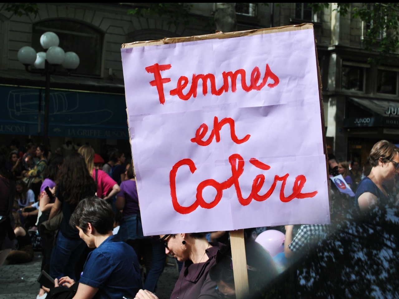Manifestation de femmes dans une rue. Au premier plan est brandie une pancarte sur lequel est inscrit Femmes en colère