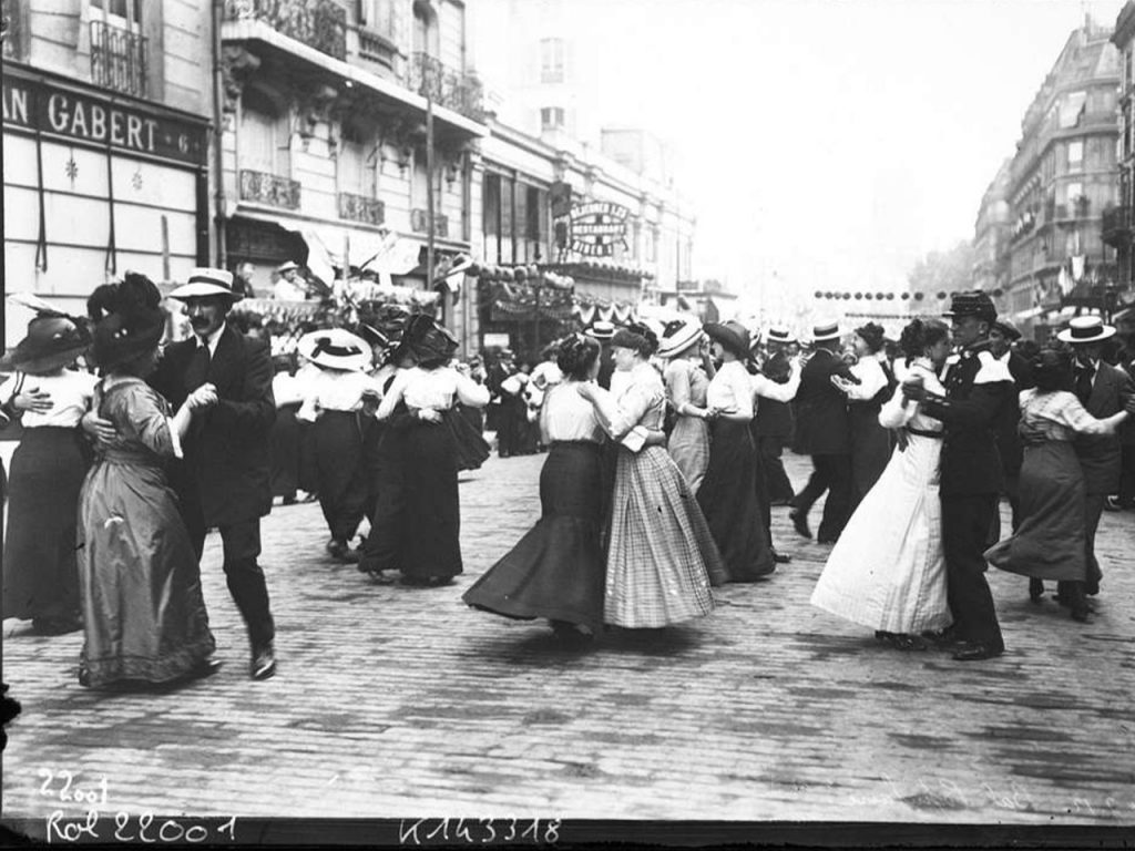 Photographie en noir et blanc lors du Bal du 14 juillet 1912 par l' Agence Rol Hommes et femmes en train de danser dans une rue