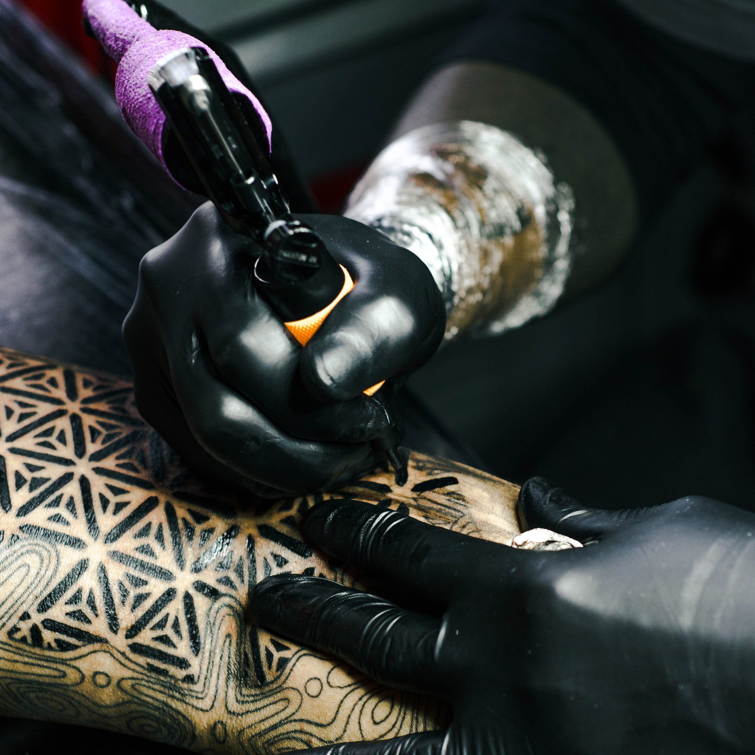 Vue d'un avant-bras tatoué avec des traits noirs par deux mains gantées de noir