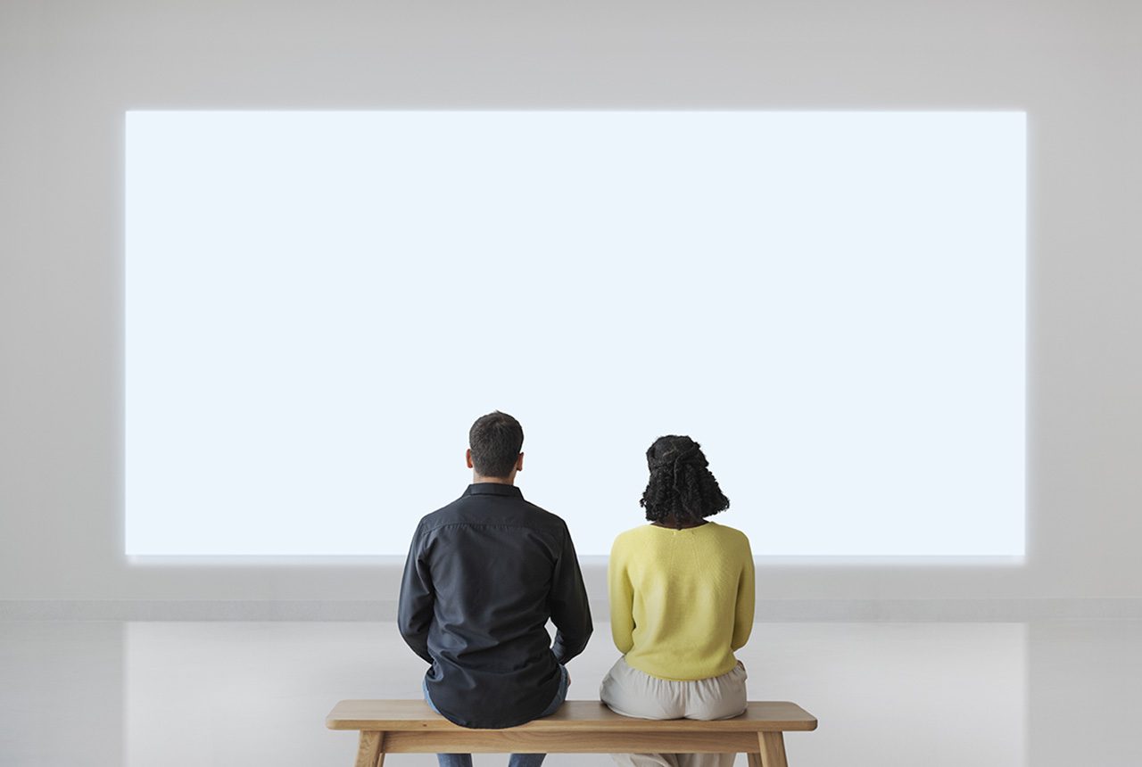 Couple assis dans un musée devant un écran lumineux blanc