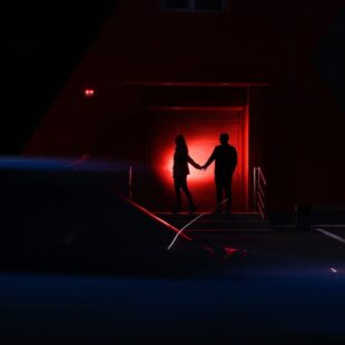 Deux silhouettes dans les ténèbres éclairées par une lumière rouge.