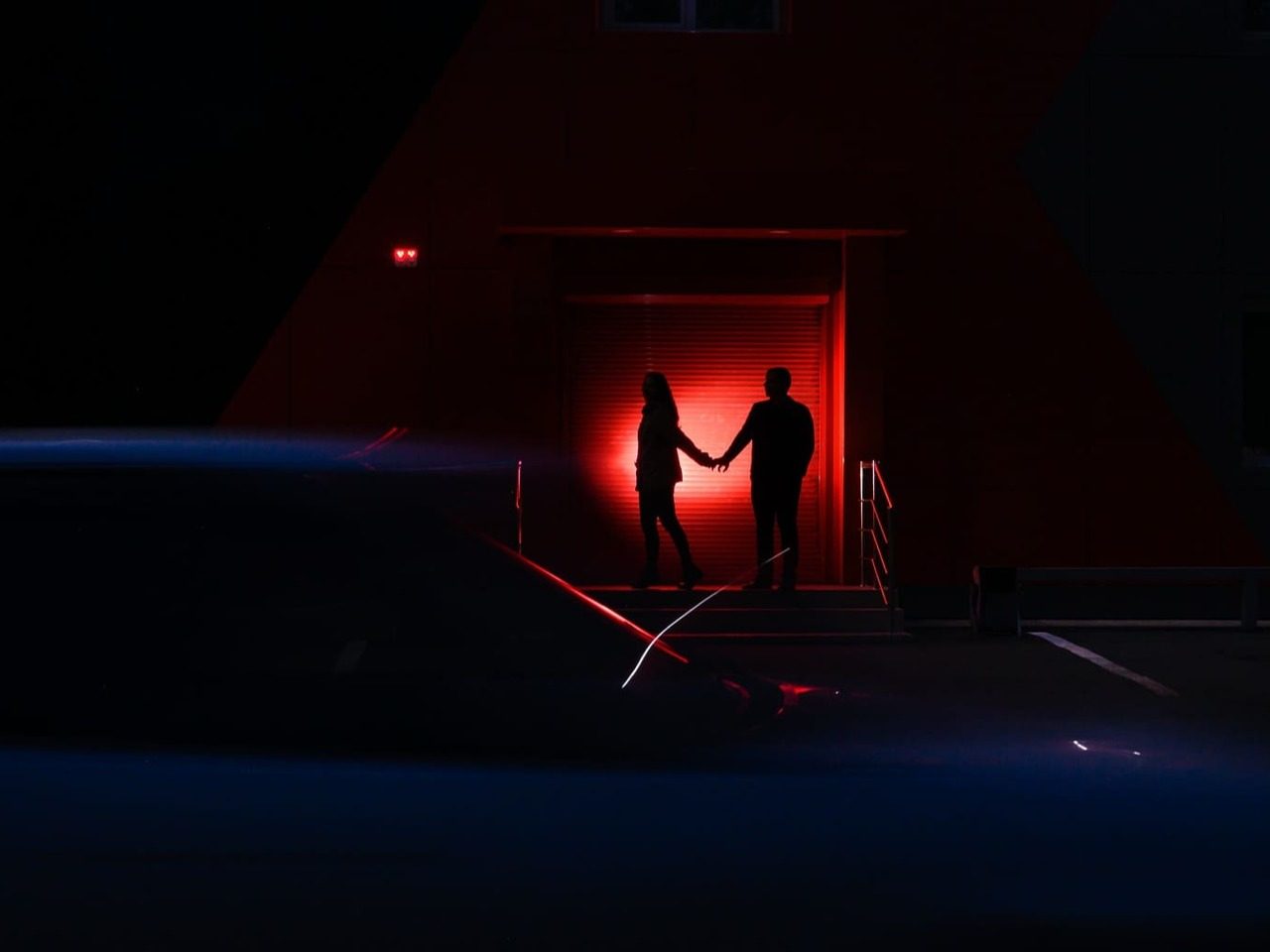 Deux silhouettes dans les ténèbres éclairées par une lumière rouge.