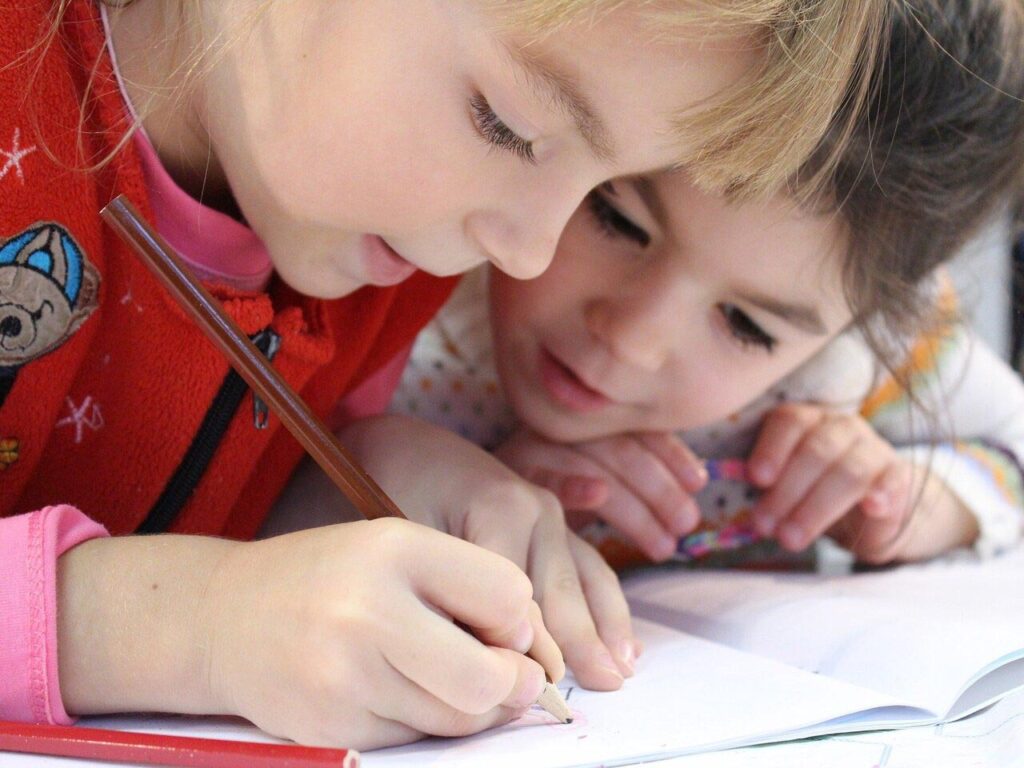 Deux enfants penchés en train de dessiner sur un cahier