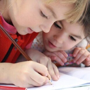 Deux enfants penchés en train de dessiner sur un cahier