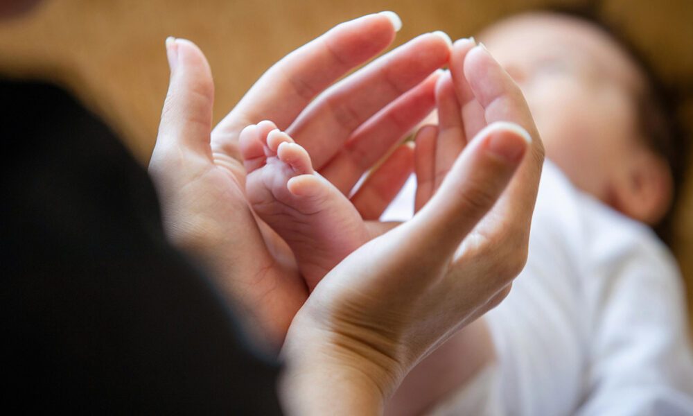 En amorce silhouette de femme, plan sur ses mains et arière-plan flou sur le bébé