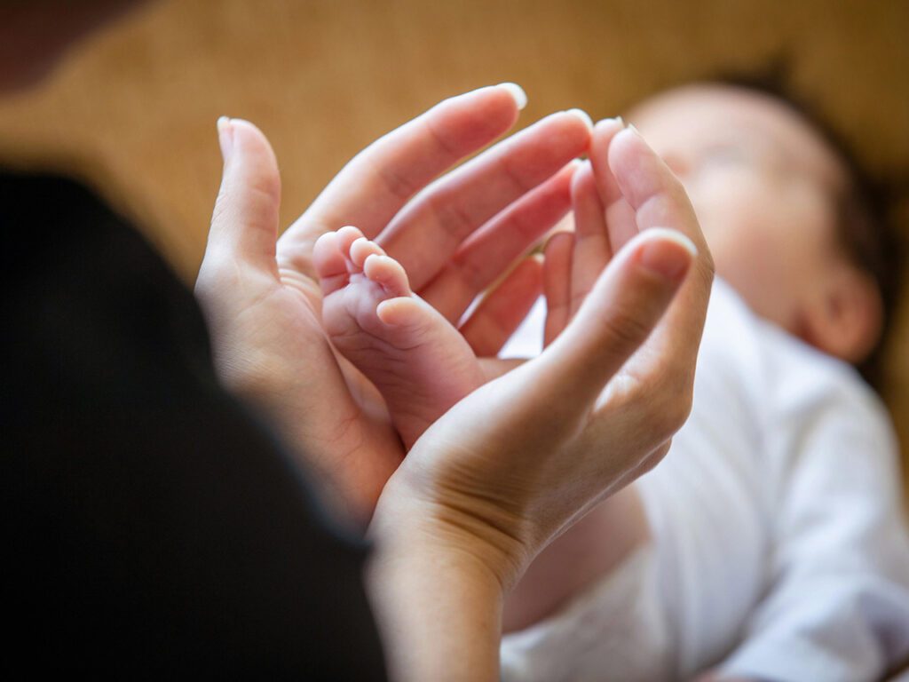 En amorce silhouette de femme, plan sur ses mains et arière-plan flou sur le bébé