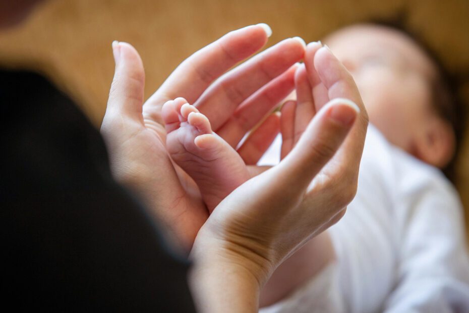 En amorce silhouette de femme, plan sur ses mains et arière-plan flou sur le bébé