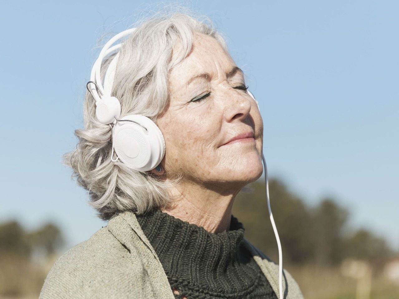 Photo de dame âgée souriante, un casque sur les oreilles