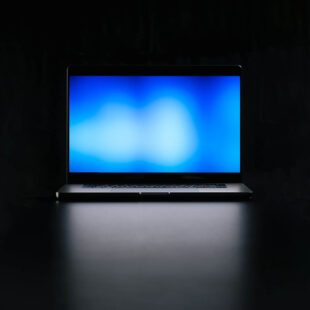 Photographie de face d'un écran d'ordinateur portable ouvert montrant un écran bleu. L'ordinateur est plongé dans l'obscurité dont la seule source lumineuse et la lumière bleue de l'écran.