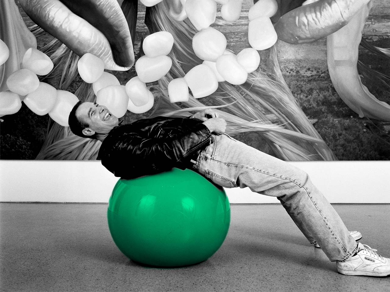 Photographie noir et blanc de Jeff Koons adossé à sur un ballon. Seul le ballon est colorisé en vert (couleur verte reprise des tulipes de JK.)