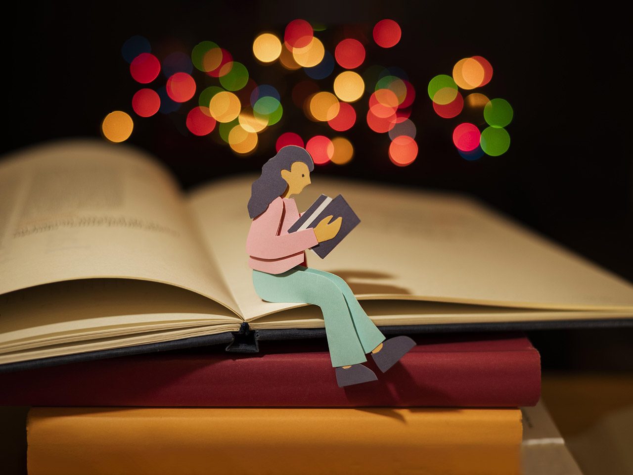 Image représentant une personne en papier assise en train de lire sur une pile de livres. En haut de sa tête se trouve des confettis lumineux de couleurs.