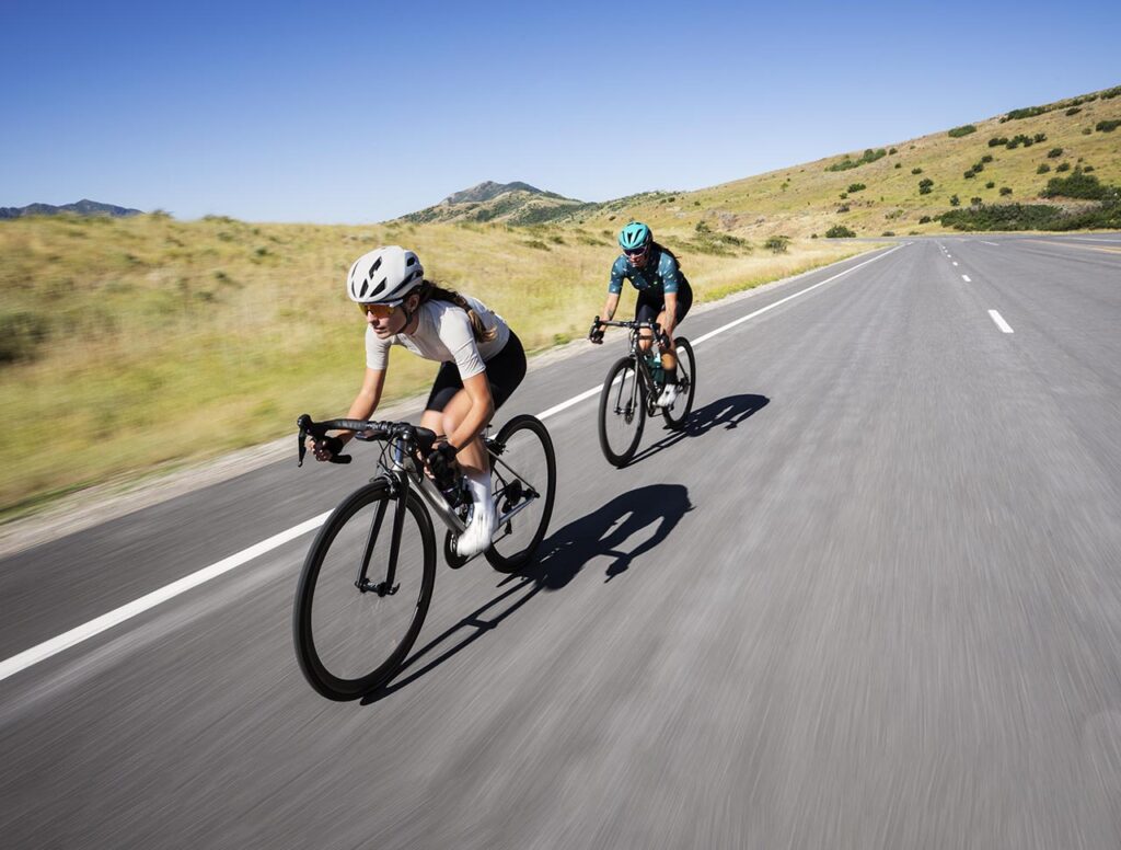 Photographie en couleurs montrant 2 cyclistes femmes allant vite sur une route de montagne.