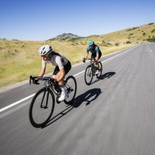 Photographie en couleurs montrant 2 cyclistes femmes allant vite sur une route de montagne.