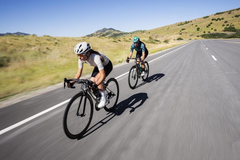 Photographie en couleurs montrant 2 cyclistes femmes allant vite sur une route de montagne.